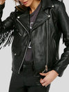 Person wearing a black leather jacket with fringe details on a plain background